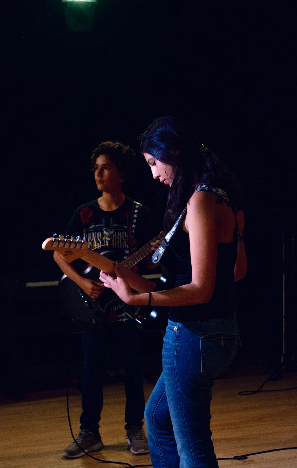 Dos guitarristas se presentan bajo luz tenue.