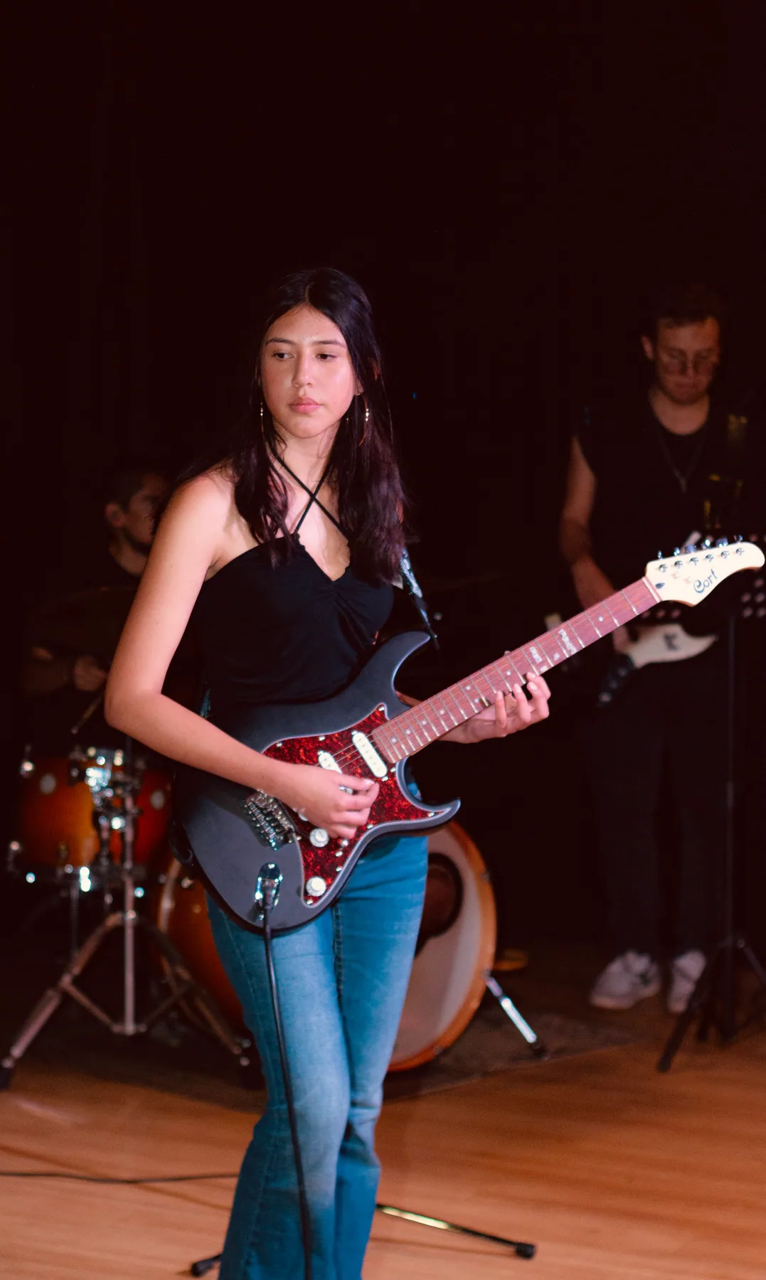 Estudiante tocando guitarra eléctrica frente a la batería.
