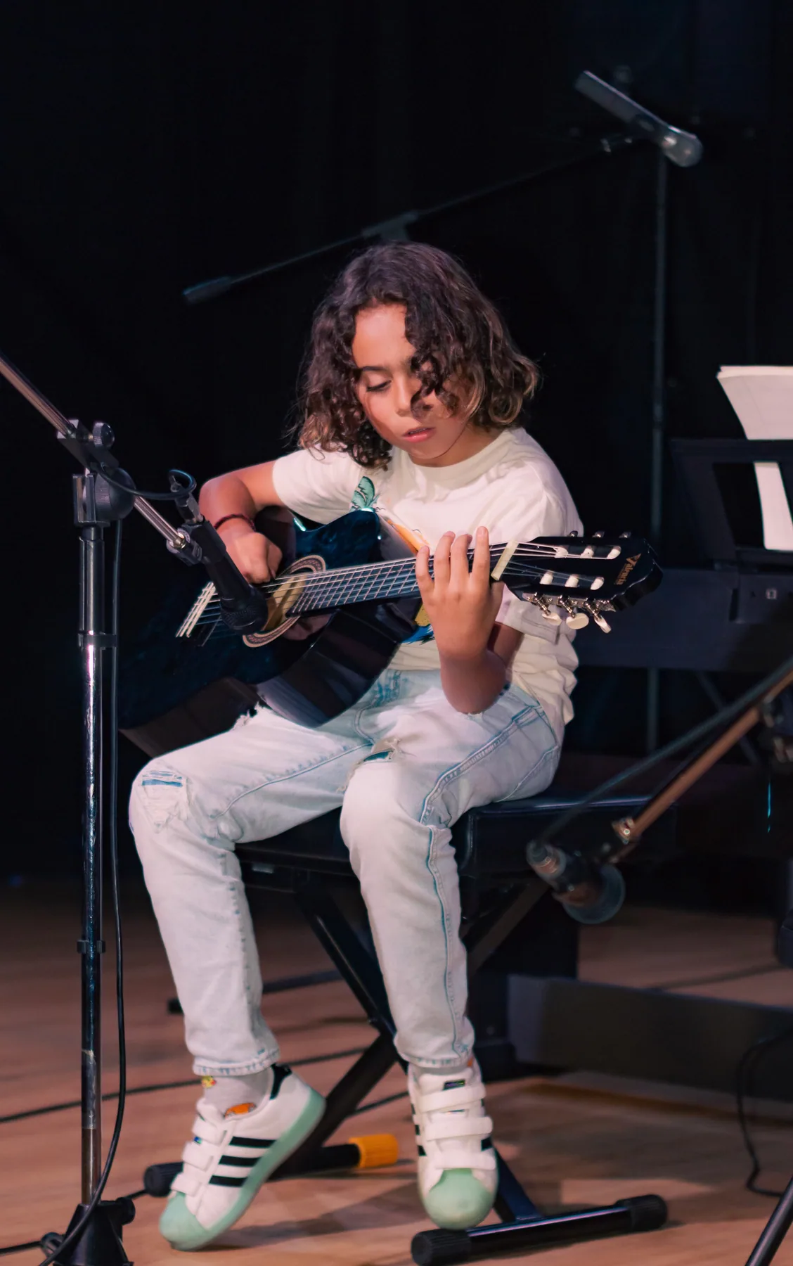Estudiante tocando guitarra acústica en el escenario.